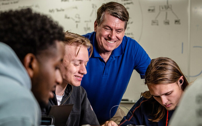 a professor smiling and talking to three students