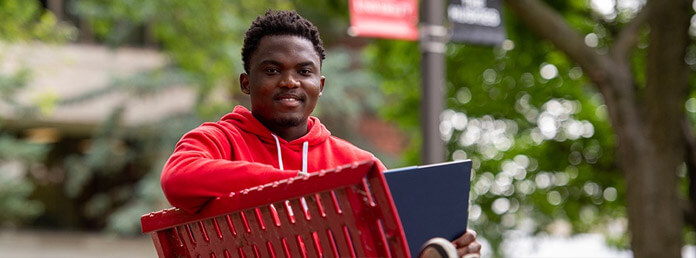 a student wearing a red hoodie sitting on a bench with a laptop