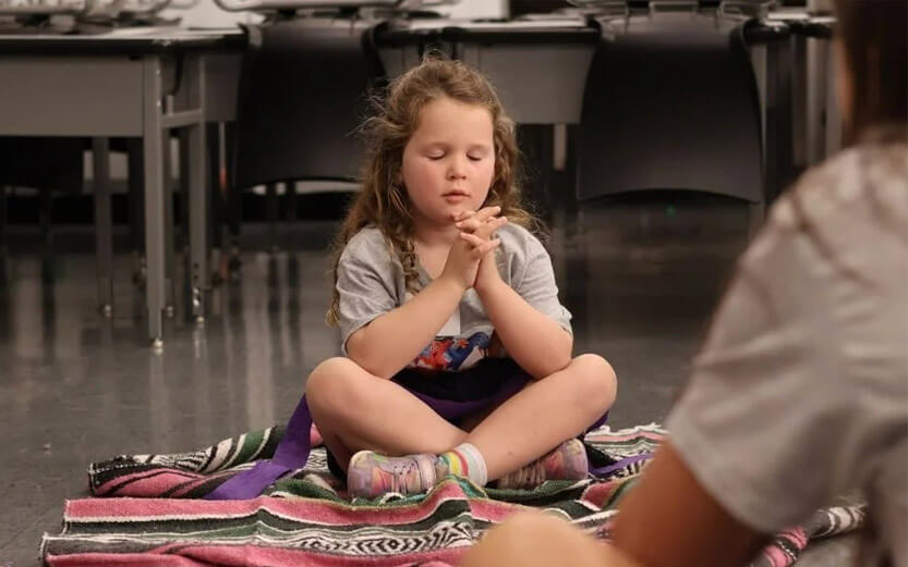 a young girl sitting on the floor with her hands folded in prayer