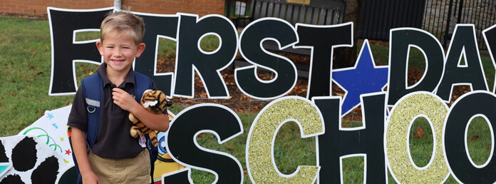 a boy posing in front of a sign on the first day of school