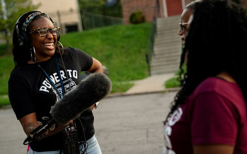 a woman operating a boom mic while smiling and talking to interview subjects