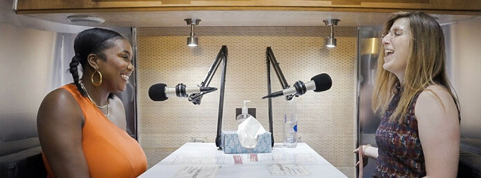 two women seated at a table with microphones in front of them during an interview