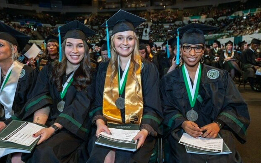 three students smiling at their graduation ceremony