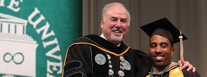 a professor with his arm around a graduate in cap and gown