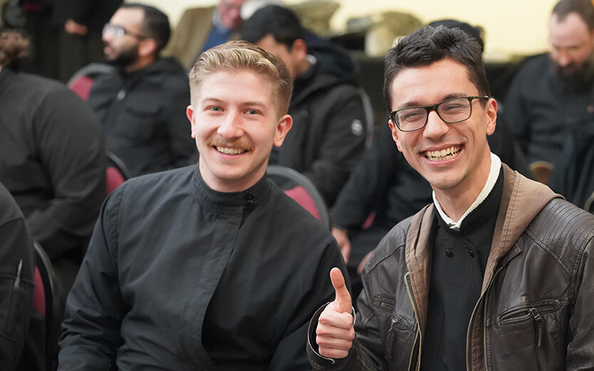 Two members of a congregation smiling. One of them giving a thumbs up.