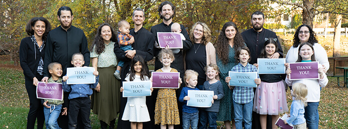 a large family posing outdoors together, with many family members holding signs that say "Thank you!"