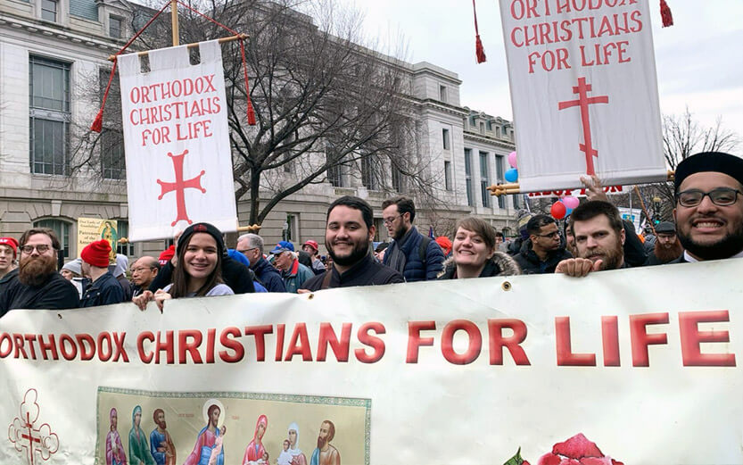 a group of people marching in a parade and holding signs that read Orthodox Christians for Life