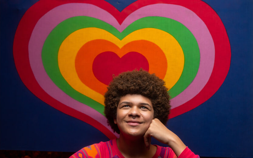 an LGBTQ+ person smiling with a colorful heart background