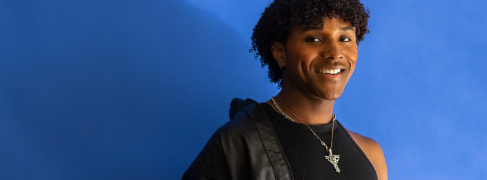 an LGBTQ+ person standing against a blue background smiling