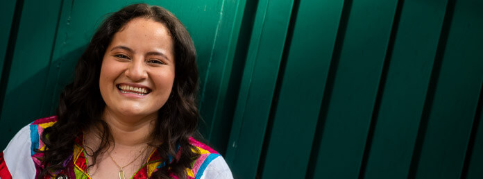 an LGBTQ+ person smiling in front of a teal wall