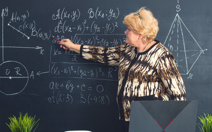 a math teacher pointing at problems on a chalkboard
