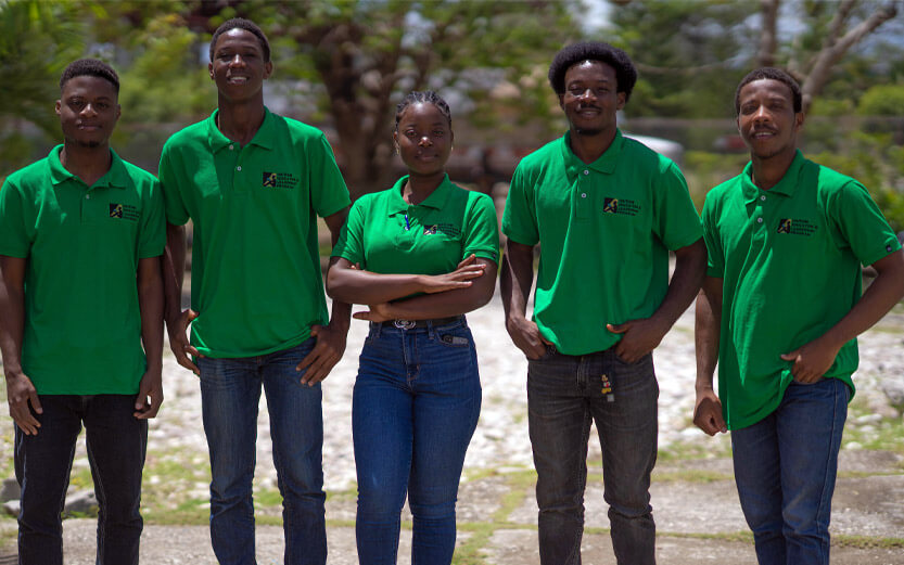 five people standing in a row wearing matching green shirts and jeans