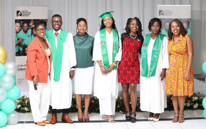 three graduates in caps and gowns with three adults standing next to them