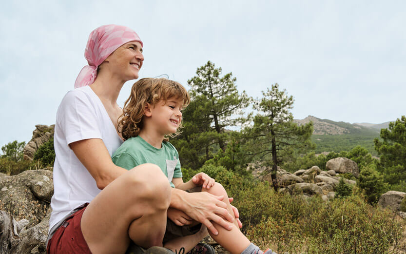 a woman wearing a head scarf sitting outdoors with her young son in her lap