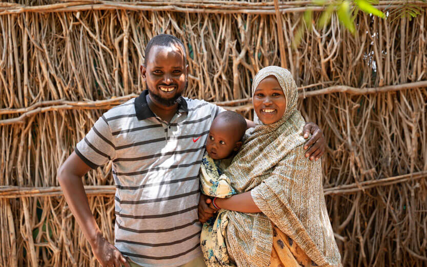 family of three in front of a wall of branches