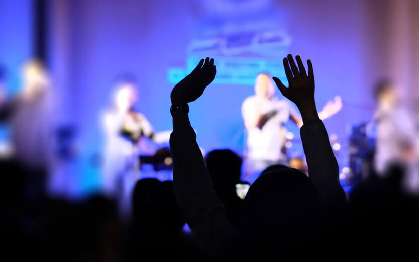 a christian music concert with the silhouette of arms reaching upwards