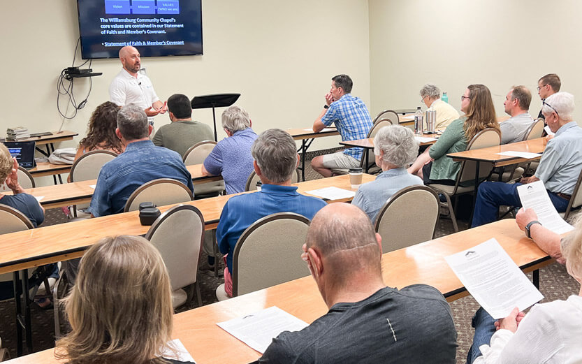 church members in a classroom setting listening to a man speak at the front of the room