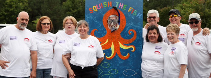 a group of people in matching white chapel tshirts and a colorful sign that reads Squish the Fish