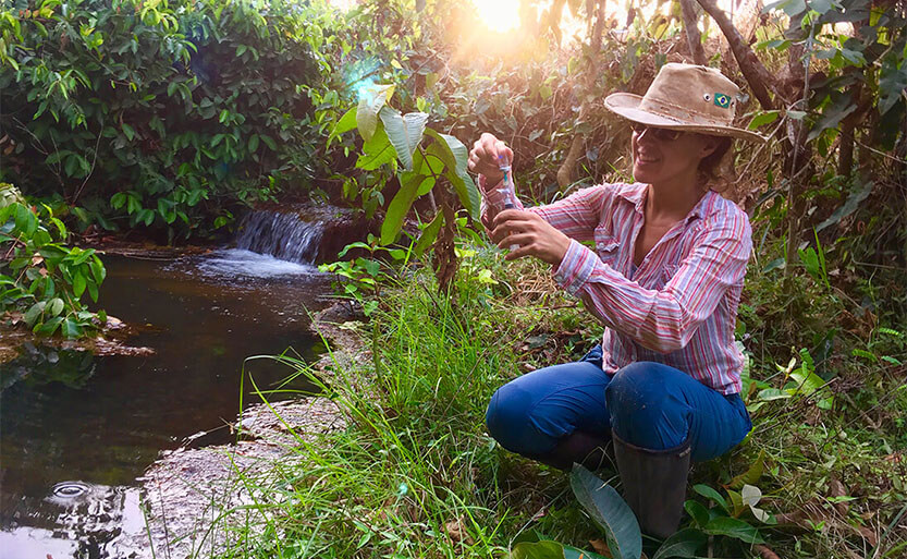 a woman in a straw hat squatting on a river bank