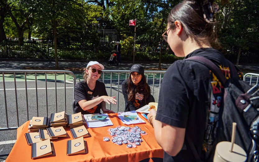 two volunteers at an information table talking to a woman