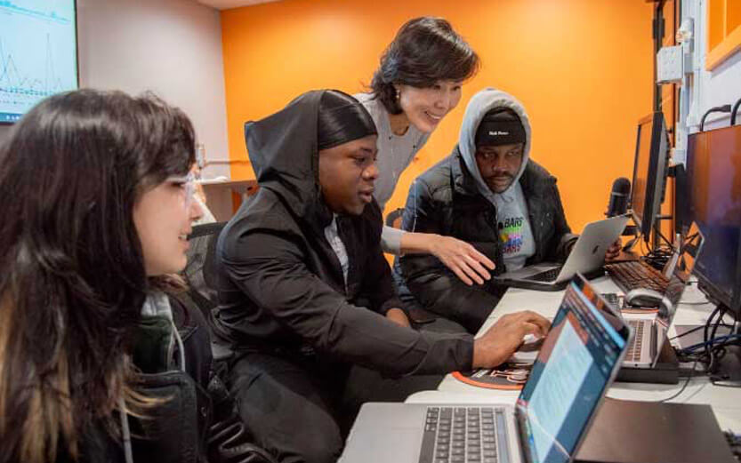 a group of students in a computer lab with a professor helping them