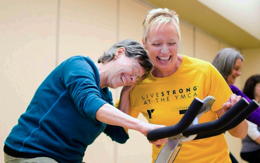 a volunteer laughing with a woman on an exercise bike