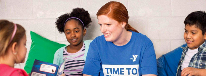 counselor smiling as a group of kids reads